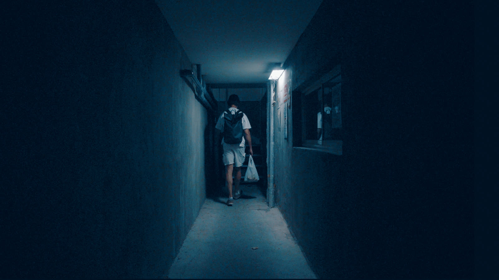 The same corridor through the Horror Blue LUT: steel-blue shadows, neutral white shirt, warm skin, the lamp still white