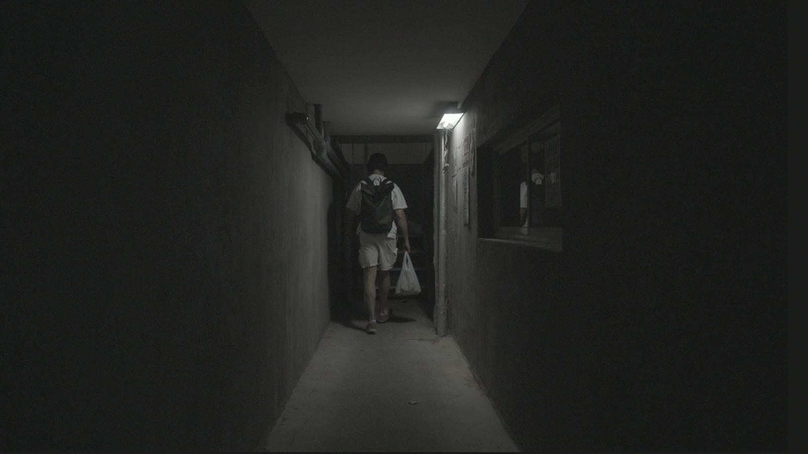 Ungraded S-Log2 footage of a man walking down a dark concrete corridor under one fluorescent tube