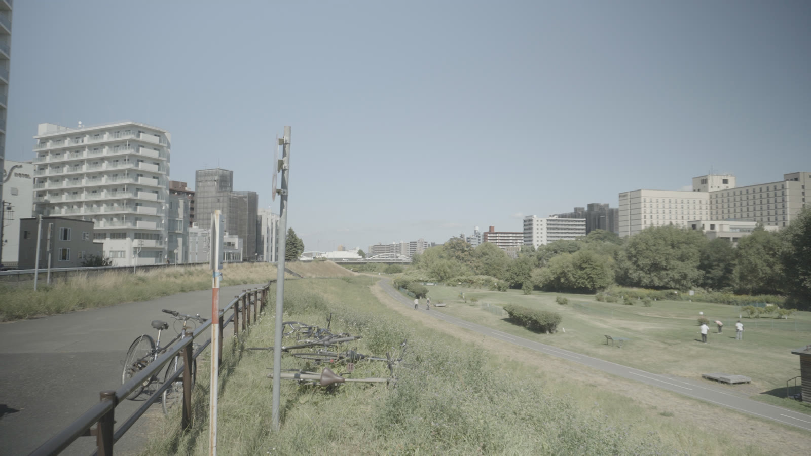 Ungraded S-Log2 footage of a riverside path with concrete apartment blocks on the skyline