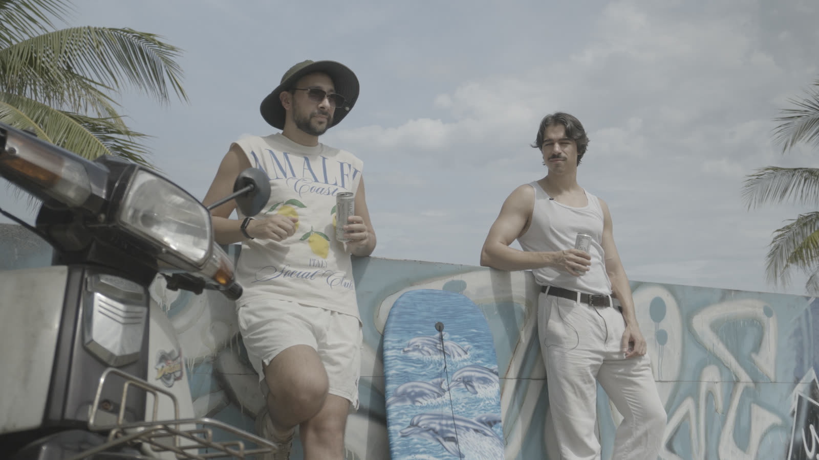 Ungraded log footage: two men with drinks against a graffiti wall, flat gray sky